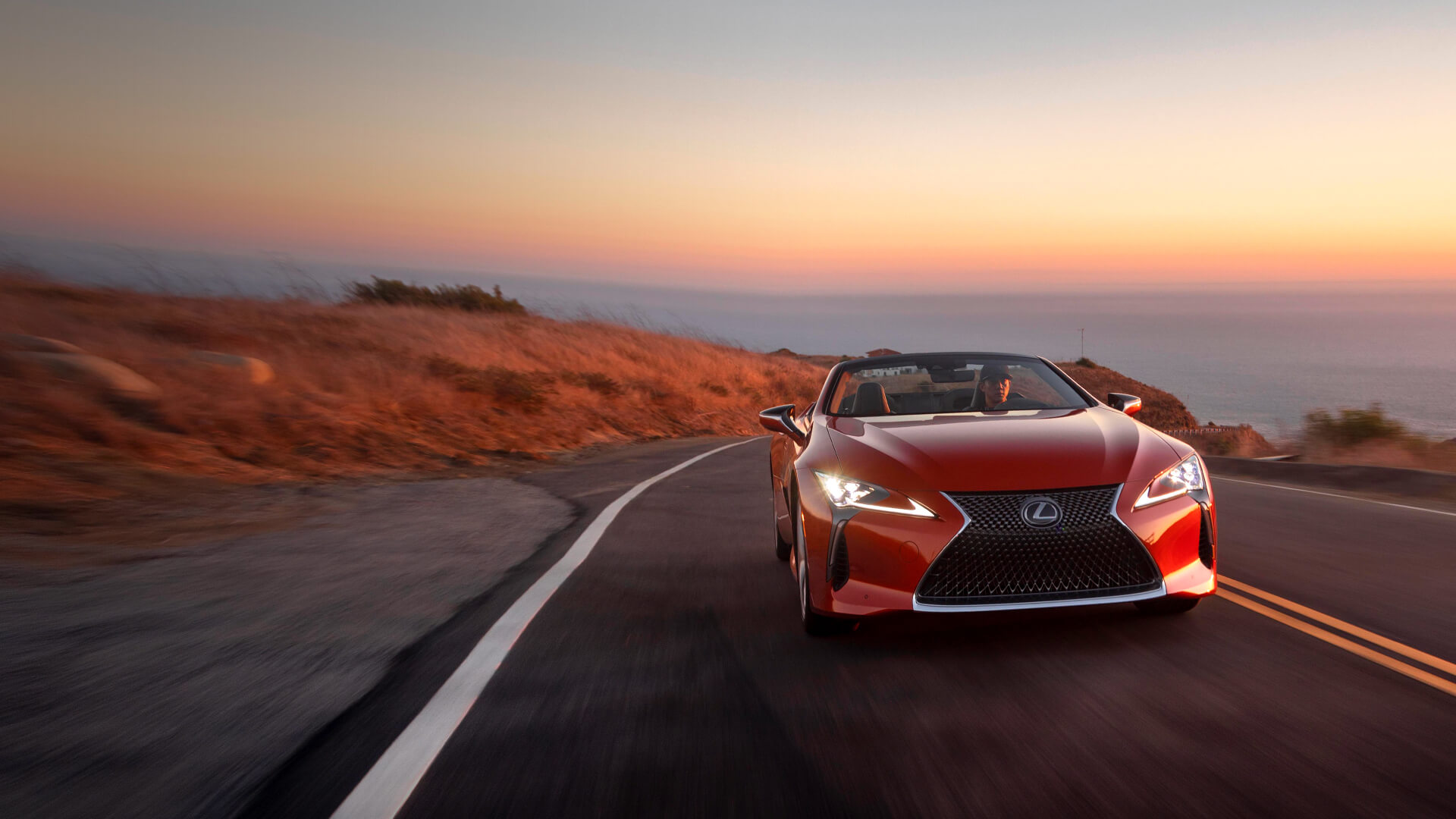 Red Lexus LC Convertible being driven on the road with the top down.​