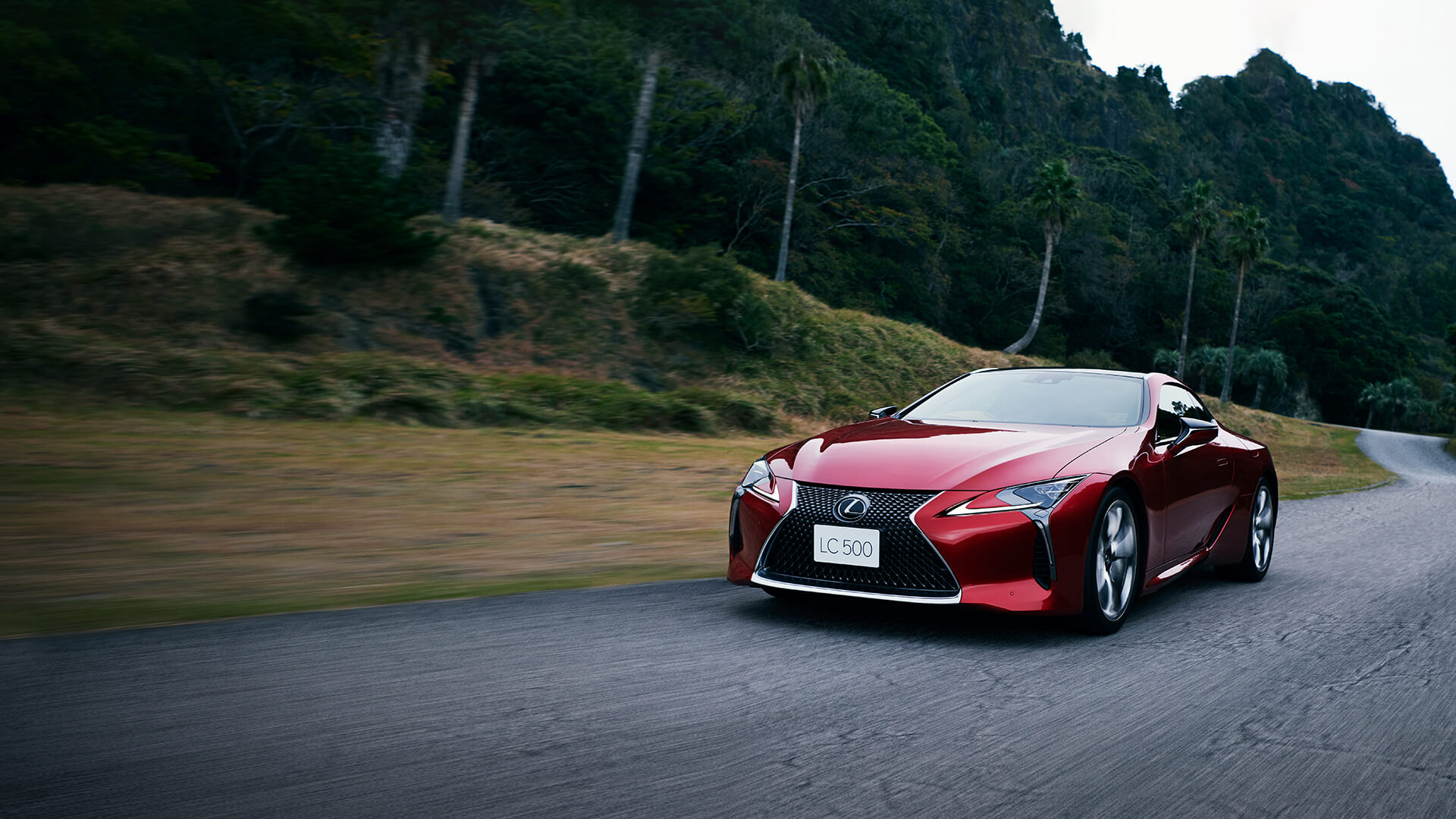 Red Lexus LC 500 being driven on the road with the top down.