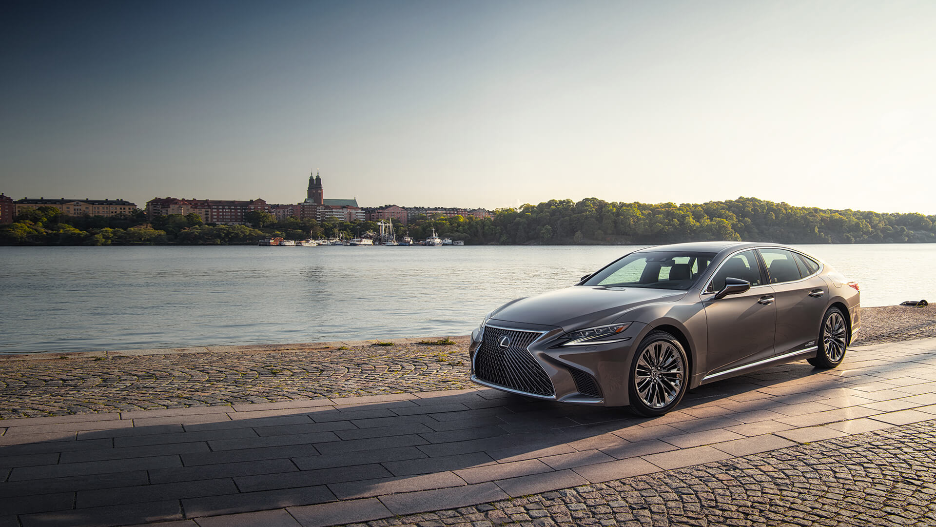 Silver Lexus LS on a stone road with the backdrop of a lake.